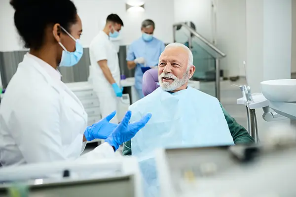 Older male patient sitting in dental chair calmly discussing his oral health with his dentist.