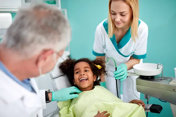 Adorable, young girl sitting in a dental chair and smiling at her older dentist and dental assistant