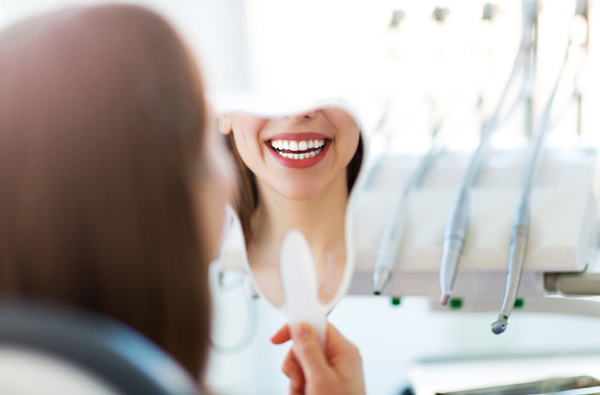 Woman looking at her smile in a mirror after getting restorative dental treatment at Djawdan Center for Implant and Restorative Dentistry