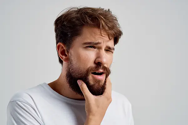 A man holding his jaw due to the pain from untreated complications of facial trauma.