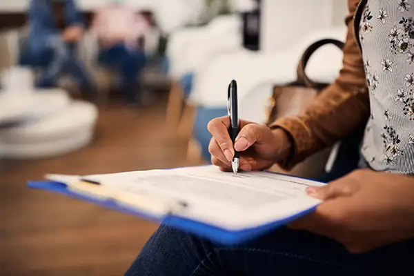 A close-up of a woman filling out insurance or financing paperwork in a waiting area.