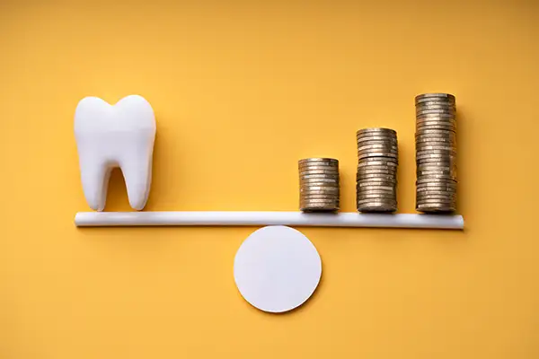 A scale balancing stacked coins on one side and a large tooth on the other side.